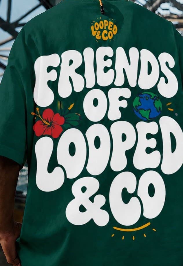 The back of a green Friends of Looped & Co tee, worn outdoors under a steel roof